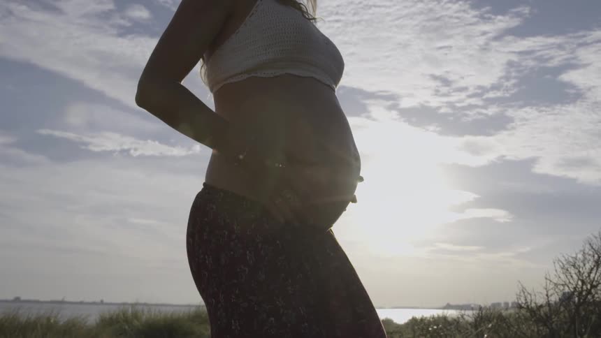 A pregnant woman holds her belly outside under the sun