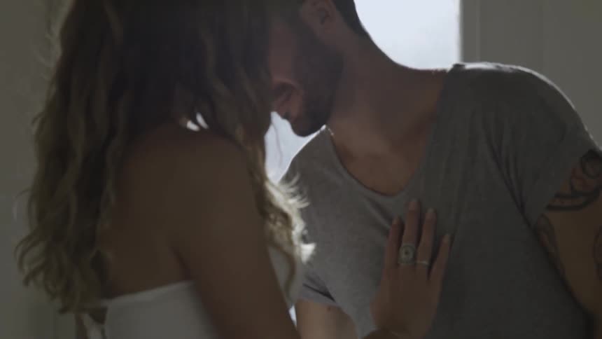 A pregnant woman caresses a man's neck and chest