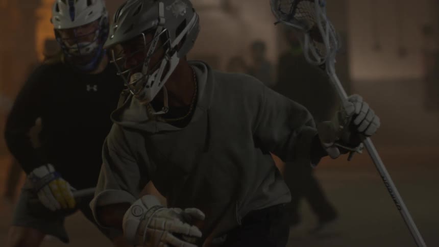 Several people play lacrosse in a dark warehouse