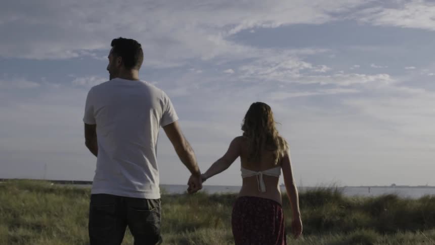Man and pregnant woman walk in a grassy field