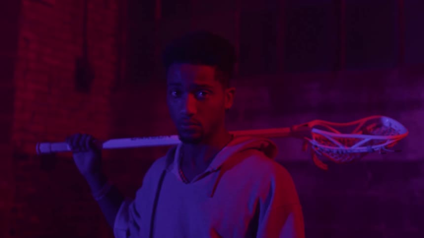 Man holds a lacrosse stick illuminated by red and blue light