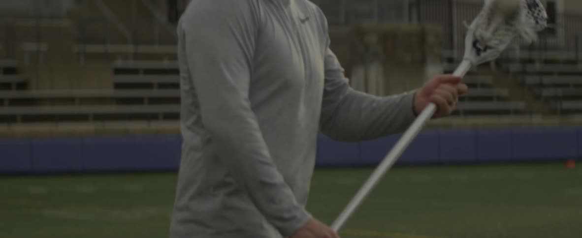 A man picks up a lacrosse ball with his stick