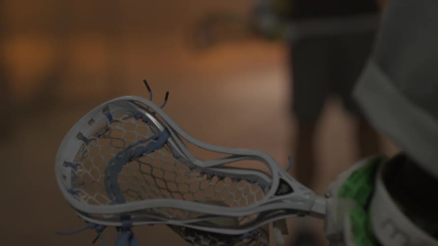 A lacrosse ball is being tossed in the net of a stick