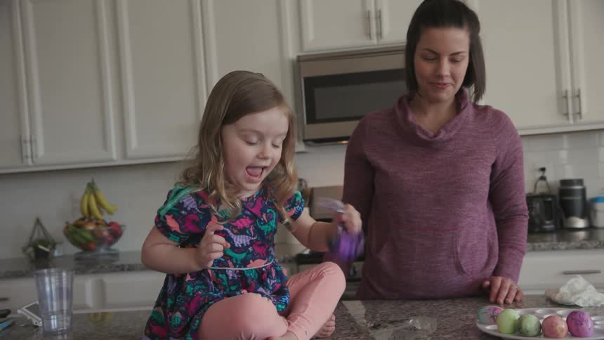A woman watches a young girl shake a bag with dye and an egg in it