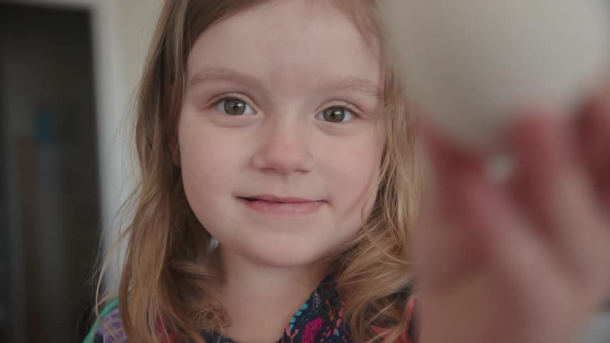 A girl holds a white egg in her hand