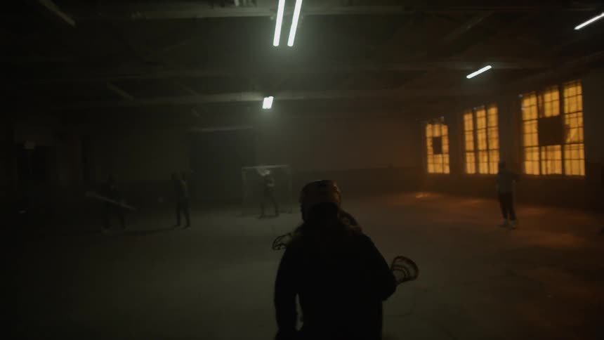Several people play lacrosse in a dark warehouse