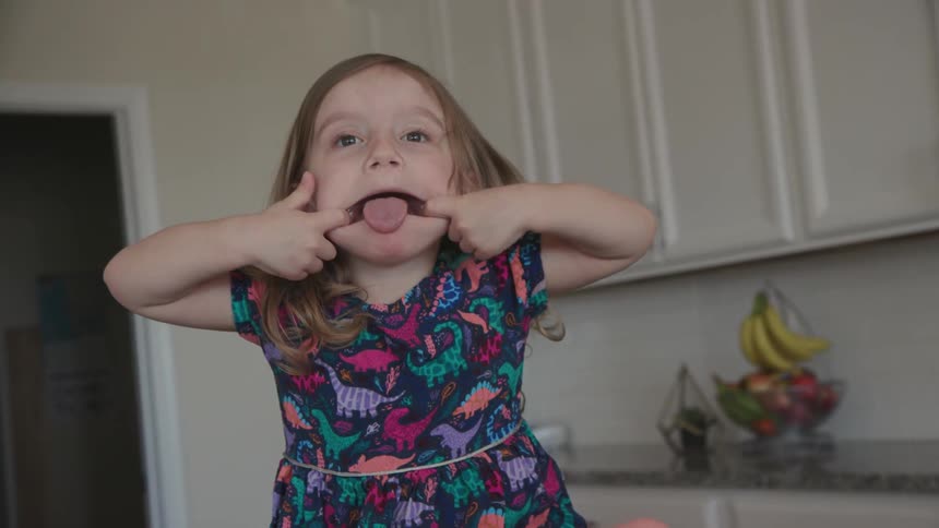 A girl sitting on a kitchen counter makes a funny face
