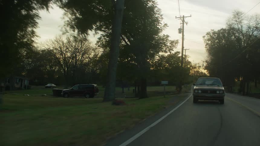 Two people ride in a car down a rural road