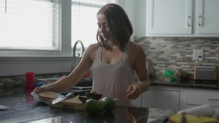 A woman prepares toast with avocado in the kitchen