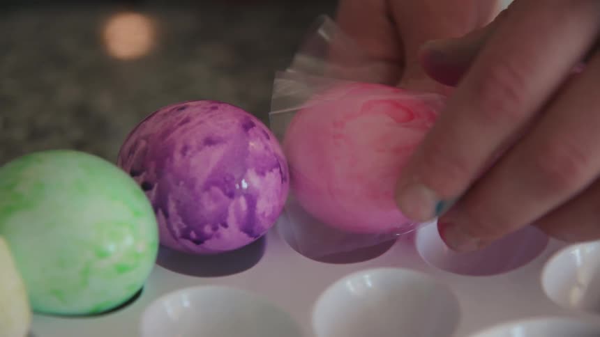 A person squeezes a colored egg out of a bag and on to a tray where a child pointed