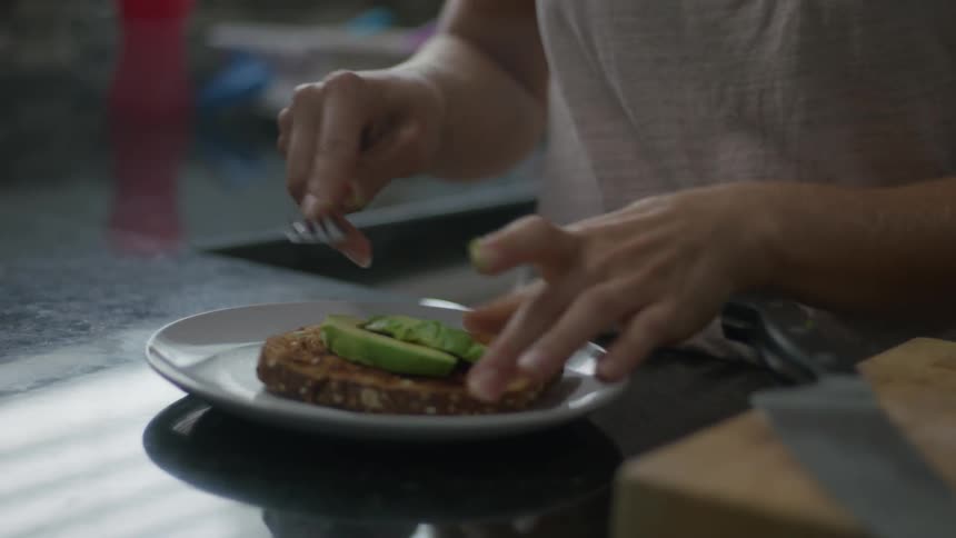 A woman puts avocado on some toast