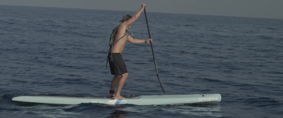 A man is on a large surfboard rowing with a paddle