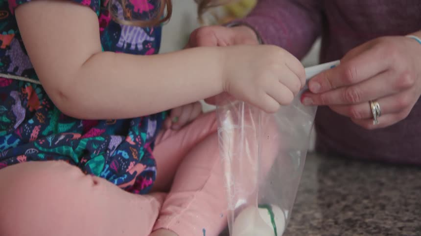 A woman and child pour dye in a bag with an egg
