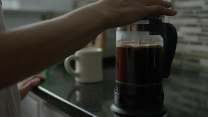 A woman is using a french press to make coffee