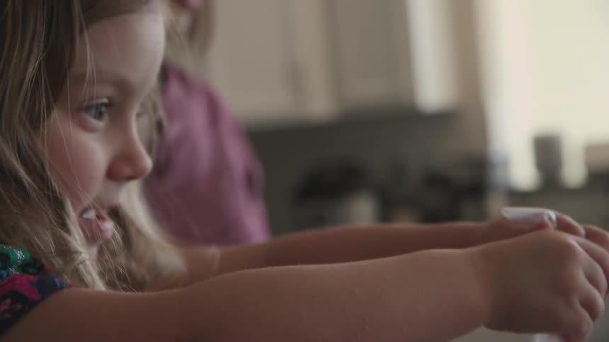 Little girl shaking egg in bag with green paint on kitchen counter