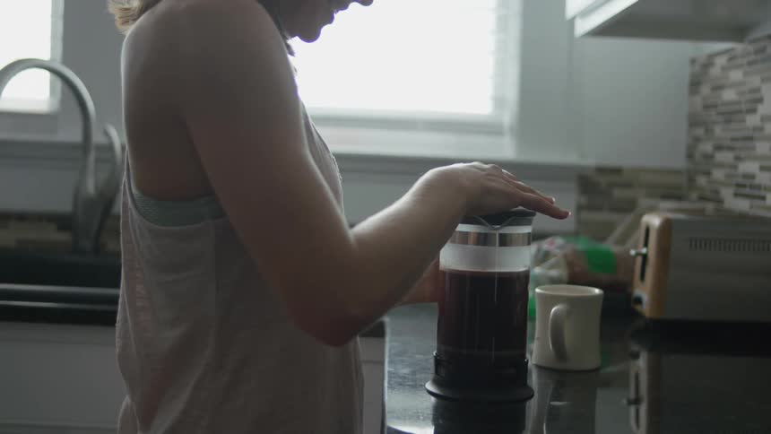 A woman is brewing coffee in the kitchen