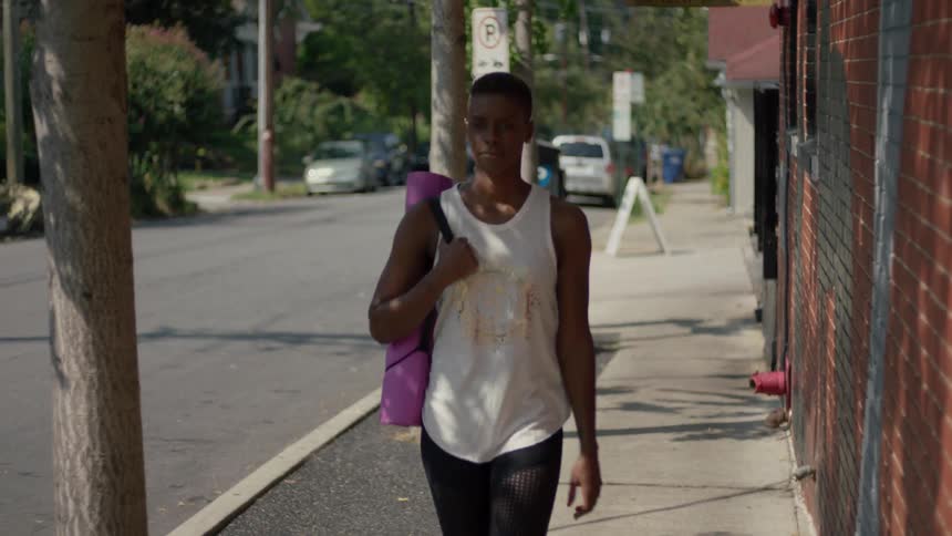A woman carries her yoga mat on a city sidewalk