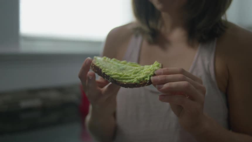 Woman eating a sandwich while wearing a tank top in a kitchen