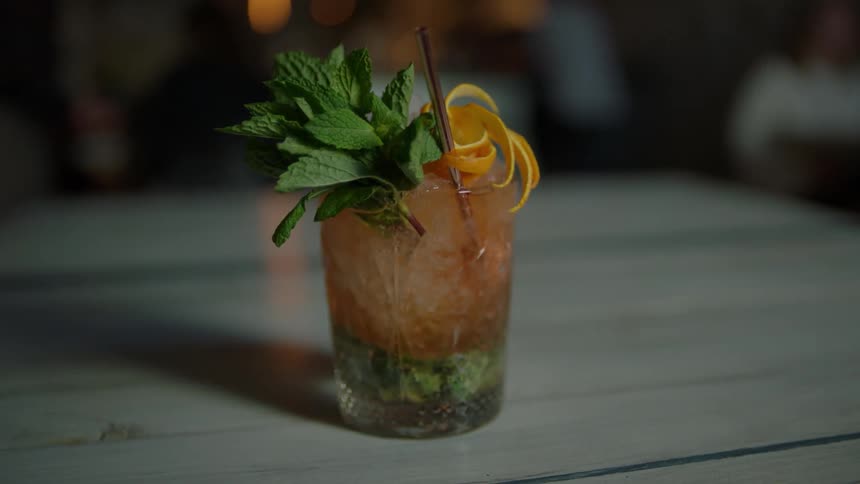 Person sets down drink on table with mint leaves and orange peels