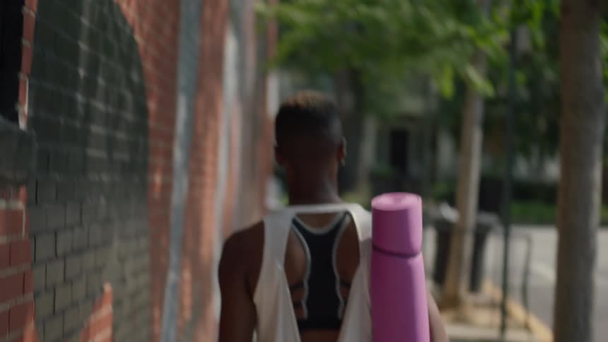 A woman carrying a purple yoga mat walks down the street