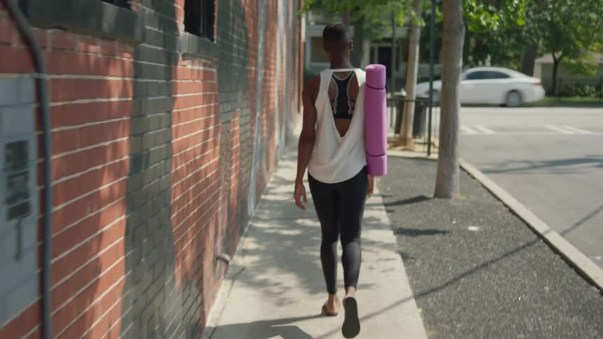 Woman with a yoga mat walking on a sidewalk