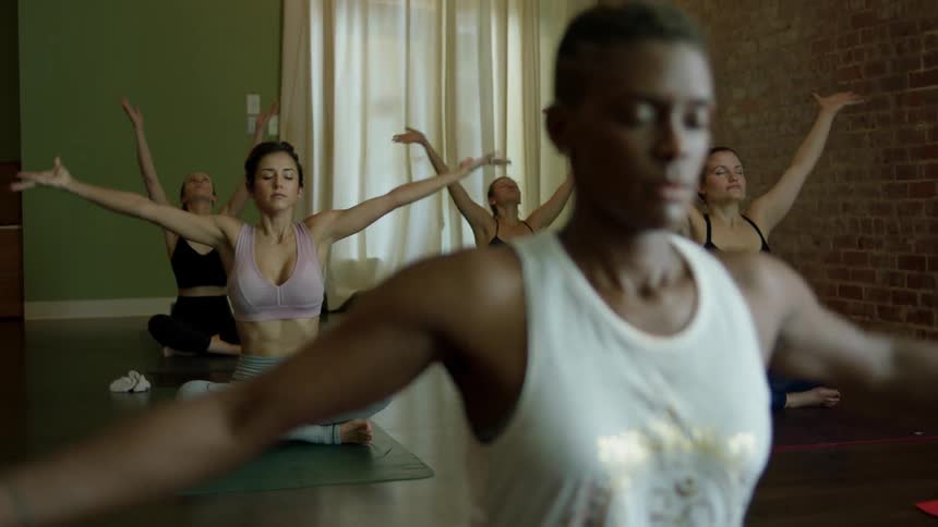 A woman sits meditating then leads to more yoga for the women behind