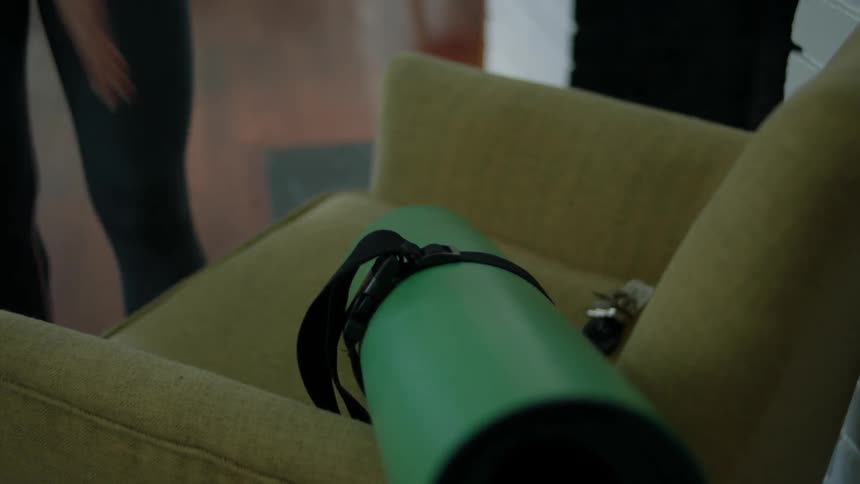 A woman picks up a yoga mat and keys from a chair