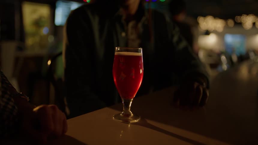 A drink is sat down in front of a man sitting at a bar