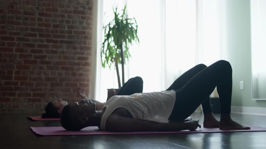 Two women are on their backs doing yoga on mats