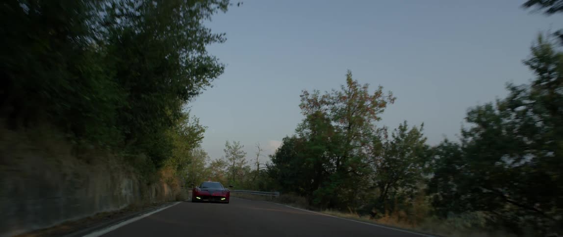 A sports car speeds down a tree lined road
