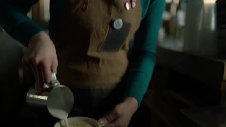 A barista pours cream into a coffee drink