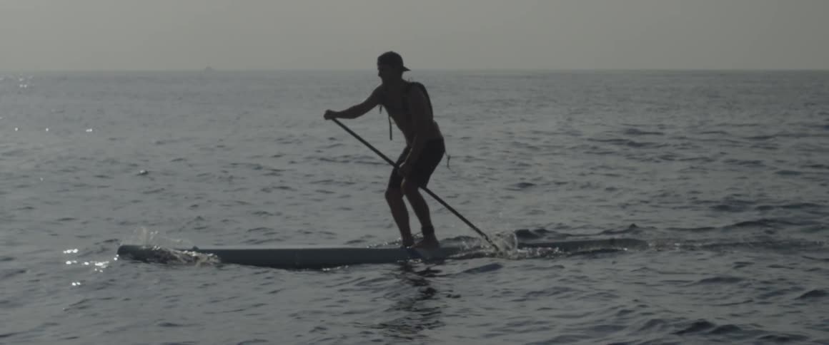 A man is paddling in the water on a large board
