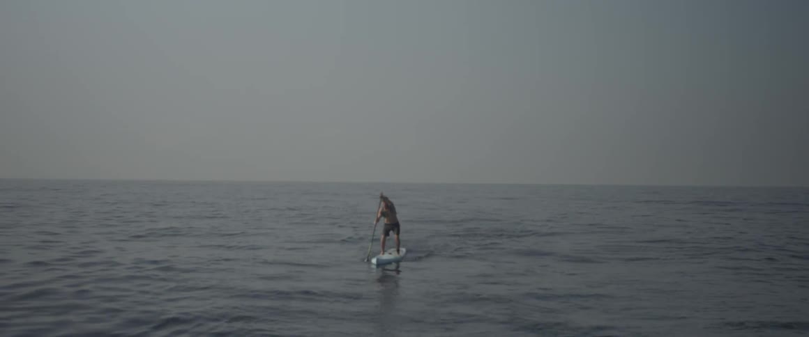 A man paddles a surfboard towards the shore