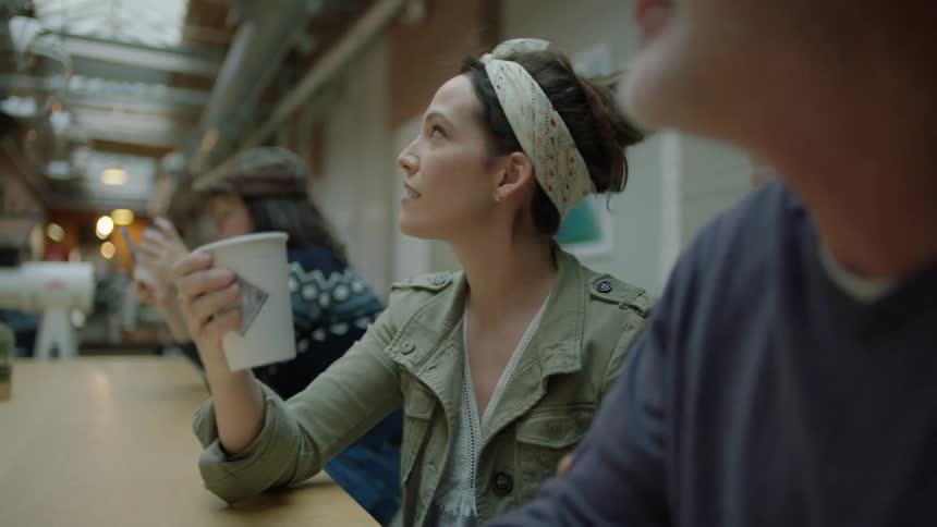 A man and woman are talking while sitting at a long counter drinking coffee