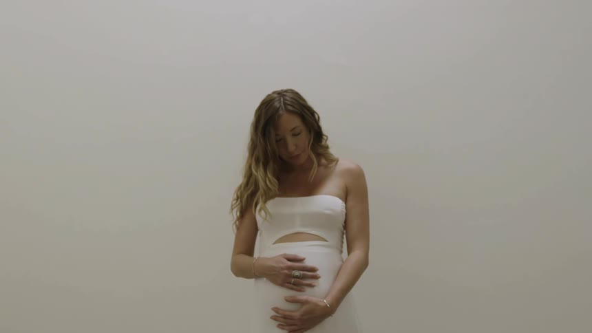 A woman touches her pregnant belly then looks up