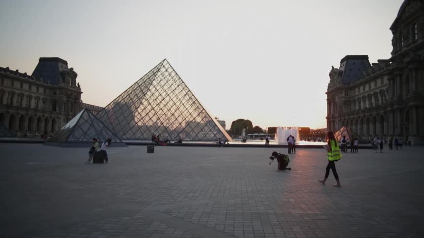 People walk across a brick pathway toward a glass pyramid