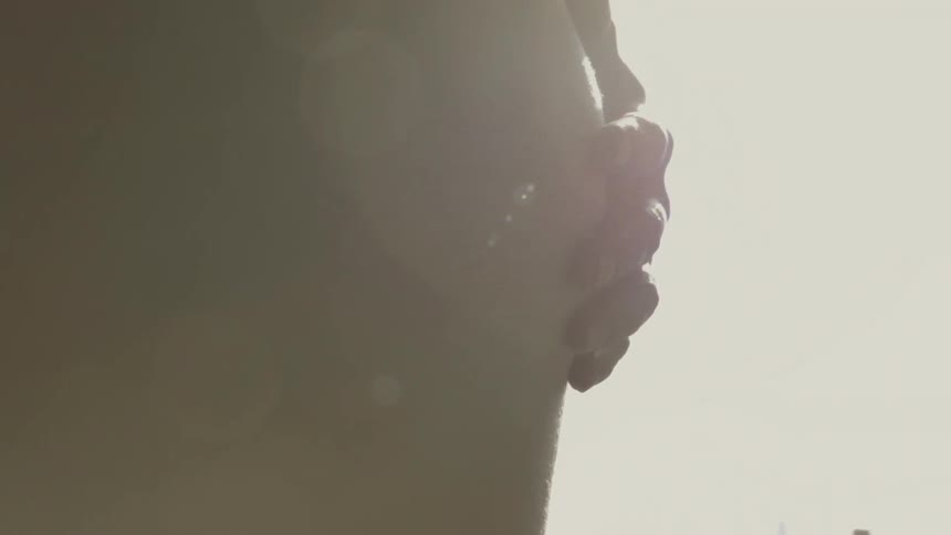 A pregnant woman rests her hand on her bare belly outside on a sunny day