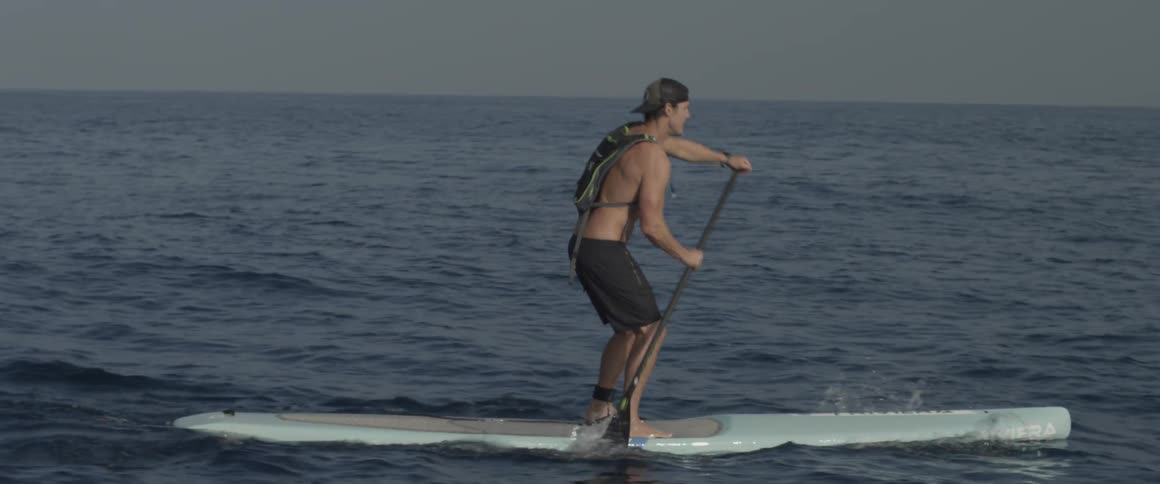 A man stands on his board and paddles on the ocean