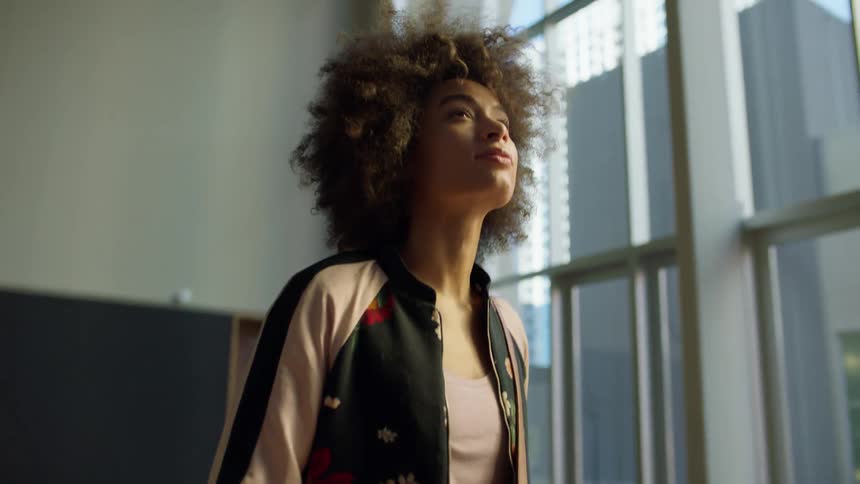 A woman stands in an empty room with tall windows