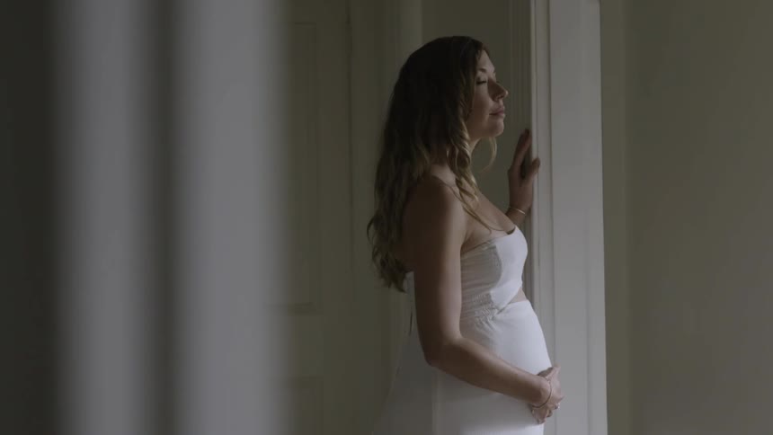 Pregnant woman in a white dress walking into a doorway