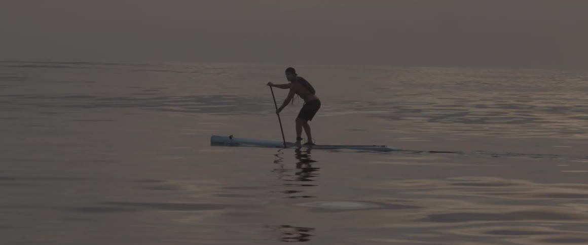 A man is slowly rowing with a paddle on a board at sunset