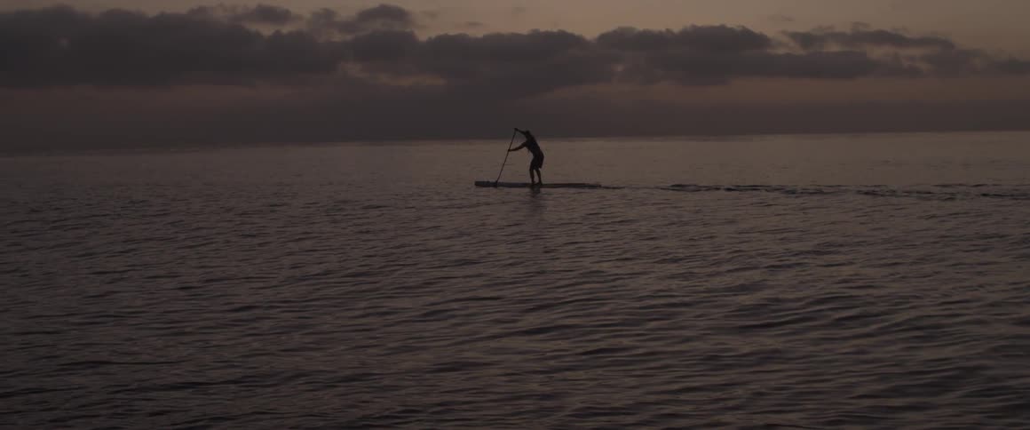 Person standing on a small raft paddles with an oar