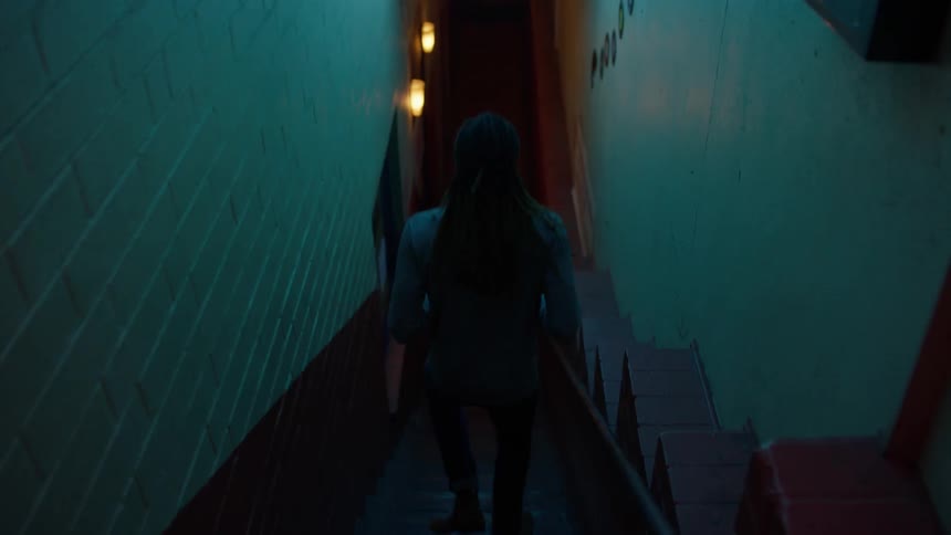A man enters a city bar at night and walks downstairs