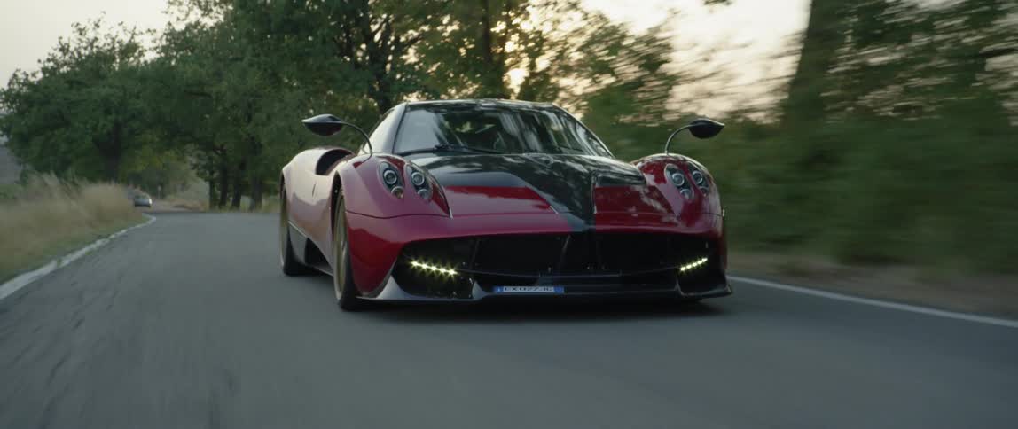 A sports car drives down a tree lined road