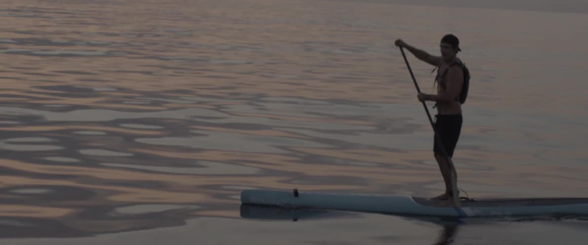 A man paddles slowly in the water at sunset