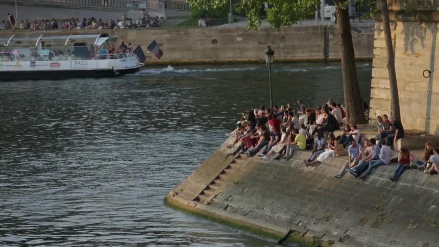 People sit around a canal as a boat passes