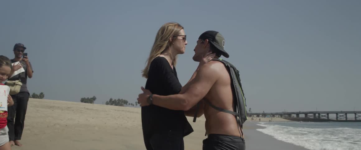 A man and woman kiss and hug on a sandy beach