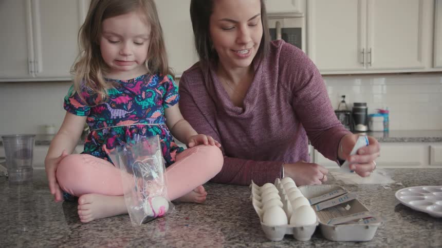 A mother helps her toddler girl dye eggs
