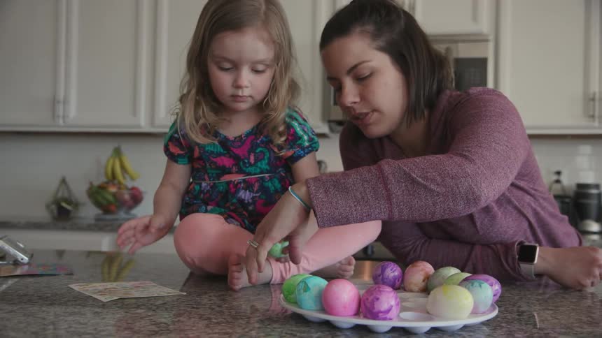 A woman helps a young girl dye eggs
