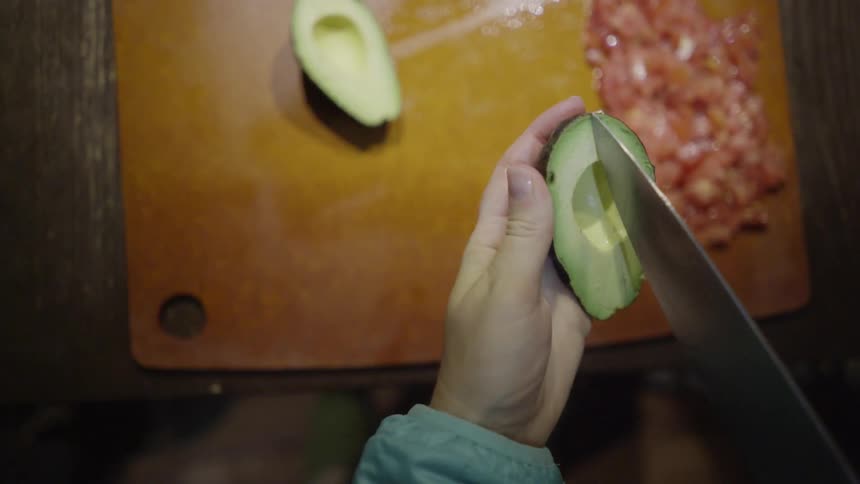 A woman cuts and carves an avocado half